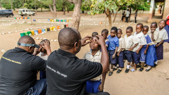 A queue of school children in uniform line up to receive an eye examination.